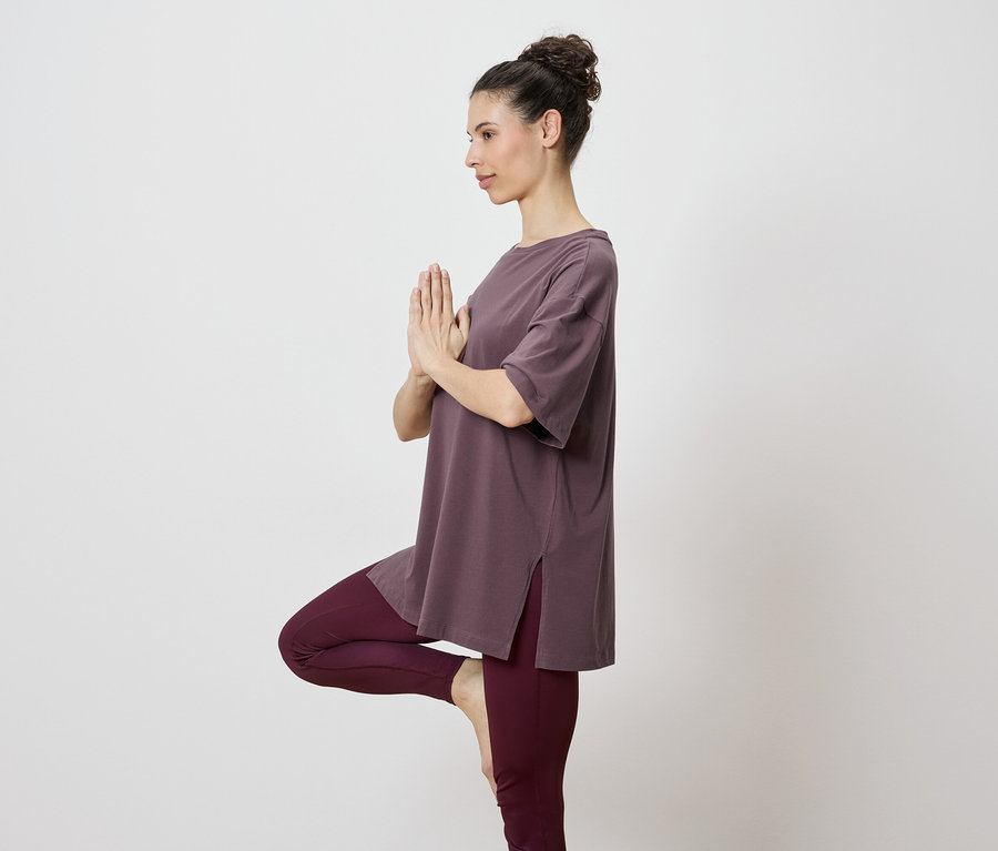Femme en haut marron et leggings faisant une pose de yoga sur une jambe.
