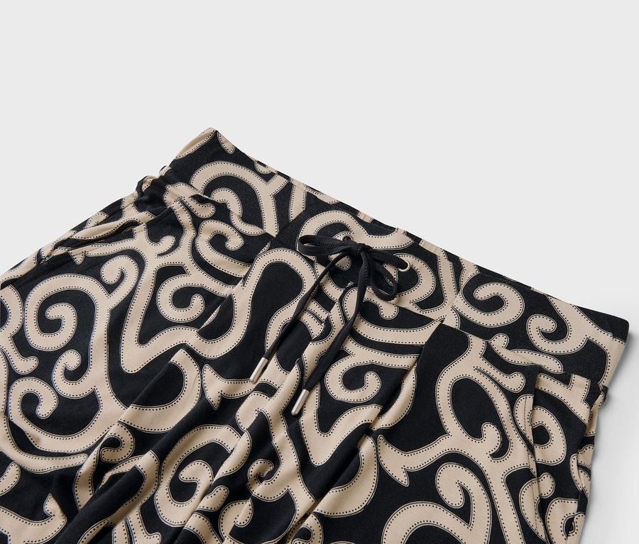 Gros plan d'un pantalon à cordon de serrage avec un motif de tourbillons noirs et beiges.