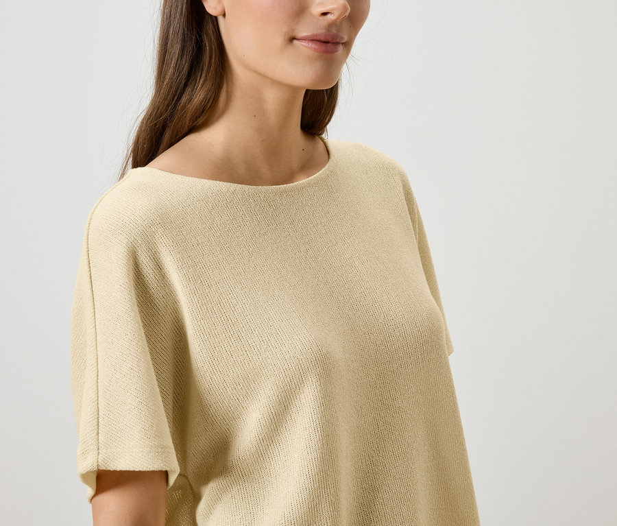 Gros plan d'une femme aux longs cheveux bruns portant un haut en tricot beige.