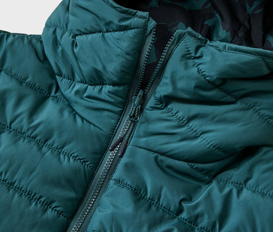 Gros plan d'une veste matelassée couleur pétrole avec capuche, partiellement ouverte, révélant une doublure à motifs.