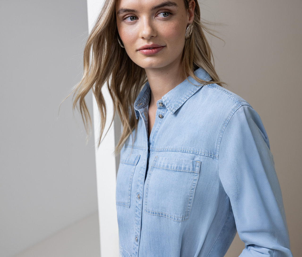 Une femme blonde porte une chemise en jean bleu clair boutonnée avec deux poches de poitrine.