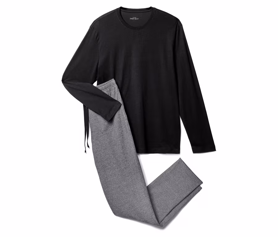 Un haut noir à manches longues est posé à côté d'un pantalon de jogging gris sur un fond blanc.