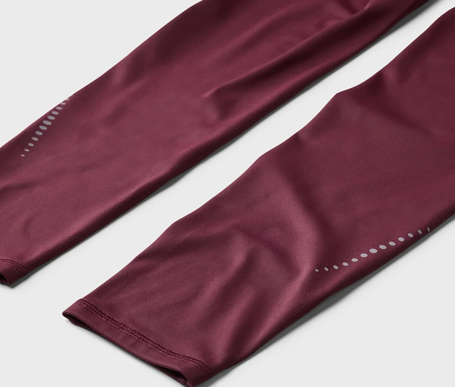 Gros plan sur un legging bordeaux avec des points réfléchissants aux chevilles.