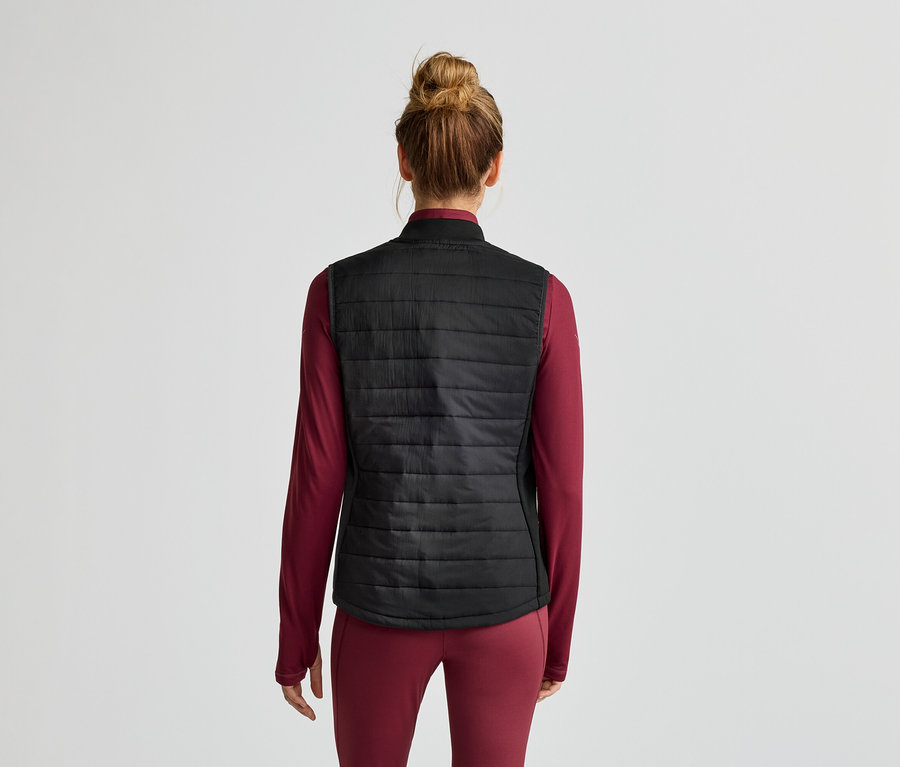 Vue arrière d'une femme avec un chignon portant un haut noir sans manches matelassé sur un haut bordeaux à manches longues.