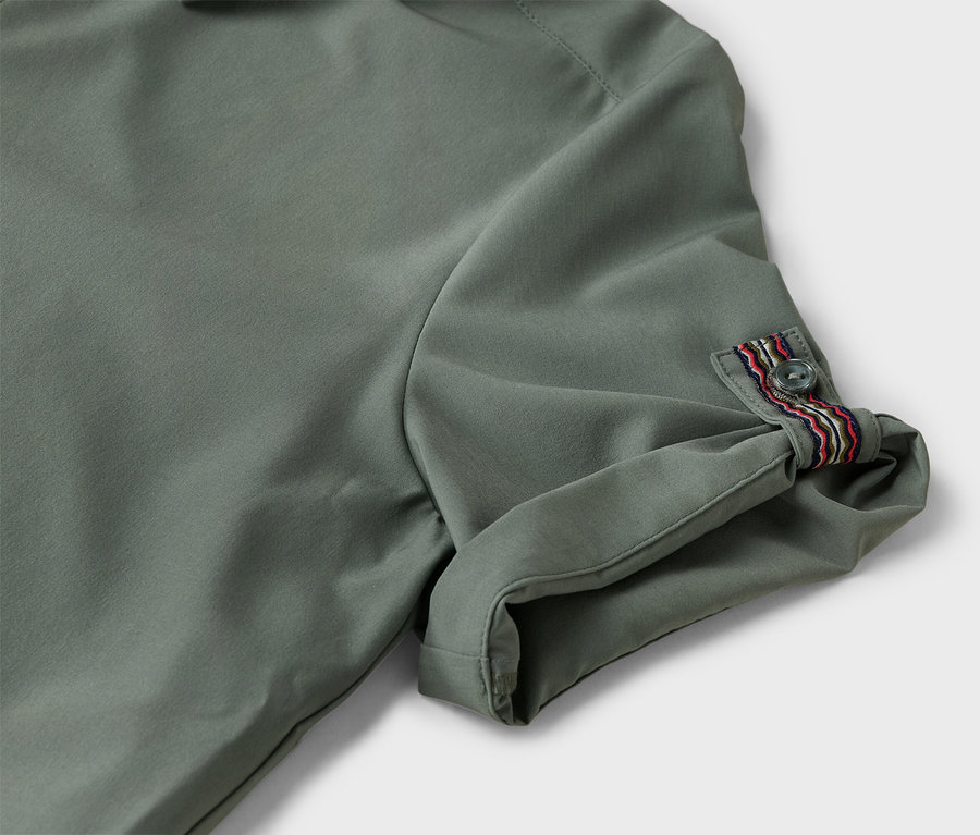Gros plan sur la manche d'une chemise vert olive, retroussée et boutonnée avec des rayures décoratives colorées.