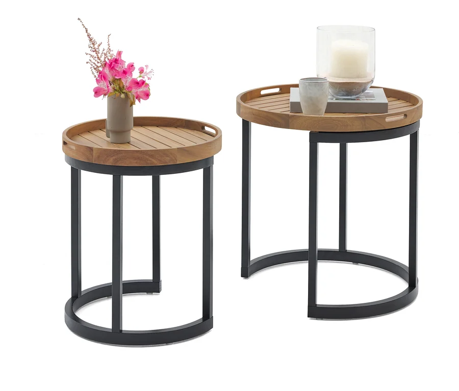 Deux tables d'appoint rondes avec plateau en bois et structure en métal noir. Sur une table, il y a un vase avec des fleurs roses, sur l'autre une bougie dans un verre et une tasse.