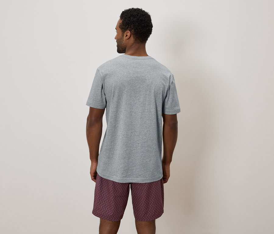 Vue arrière d'un homme portant un t-shirt gris et un short à motifs sur un fond neutre.