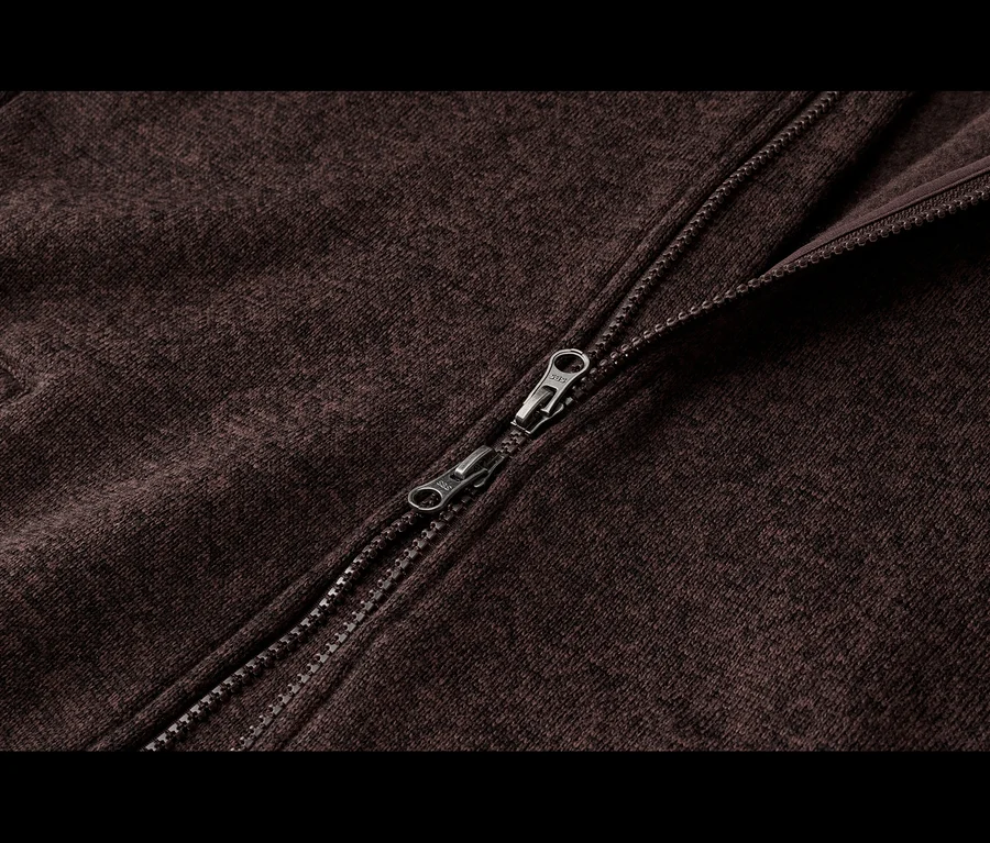 Gros plan d'un tissu tricoté marron chiné avec une fermeture éclair métallique partiellement ouverte en diagonale.