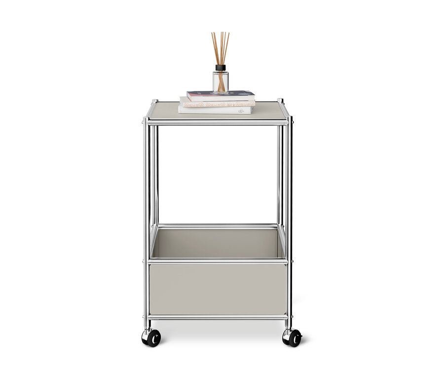 Table basse en métal « CN3 » gris clair sur roulettes avec deux étagères, dessus des livres et un diffuseur de parfum.
