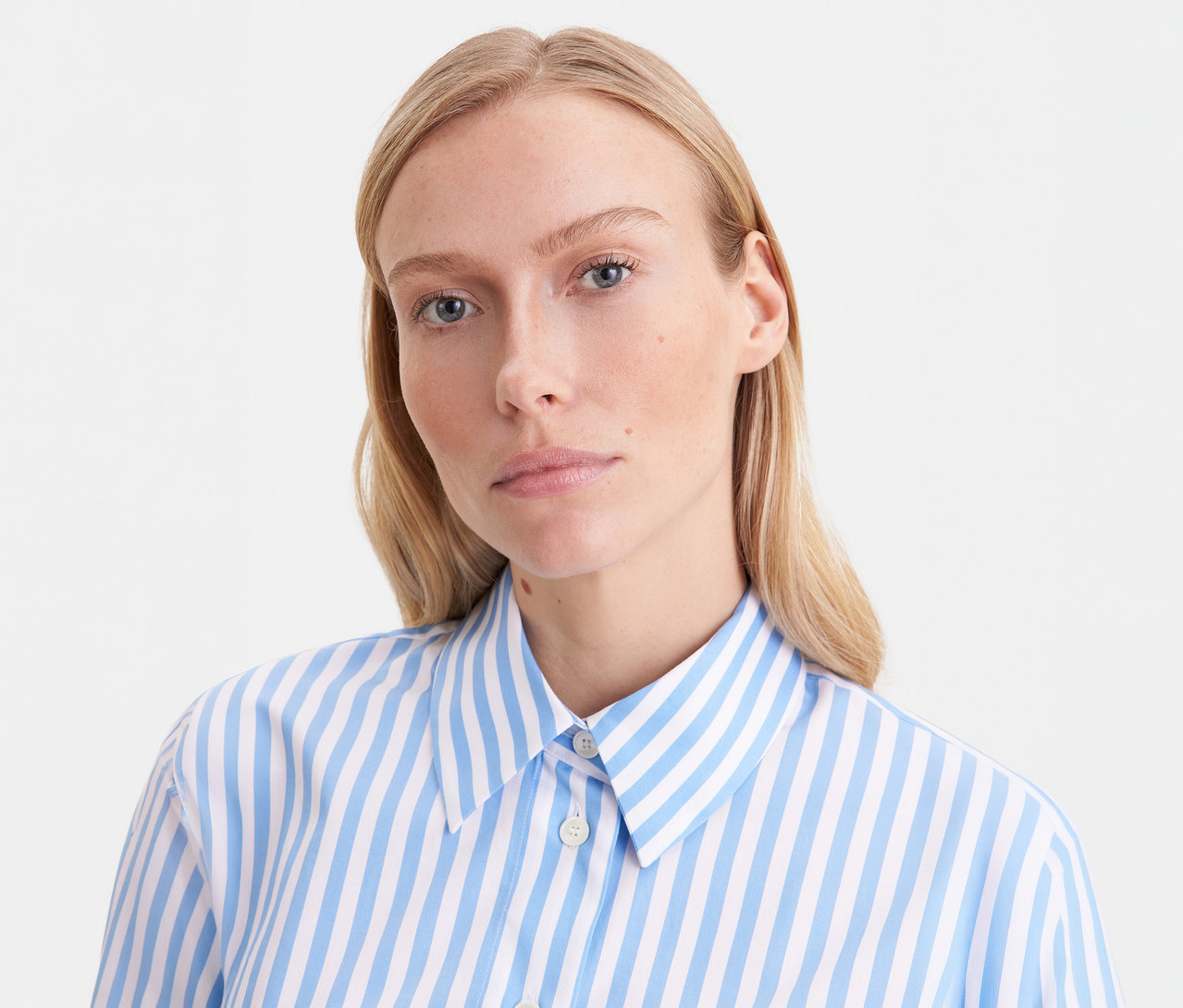Femme blonde portant un chemisier oversize Seidensticker bleu et blanc rayé, regardant l'appareil photo.