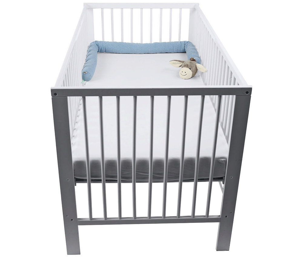 Lit bébé blanc et gris avec un matelas blanc, un tour de lit serpent bleu à motifs le long d'un côté et une petite peluche âne à la tête.