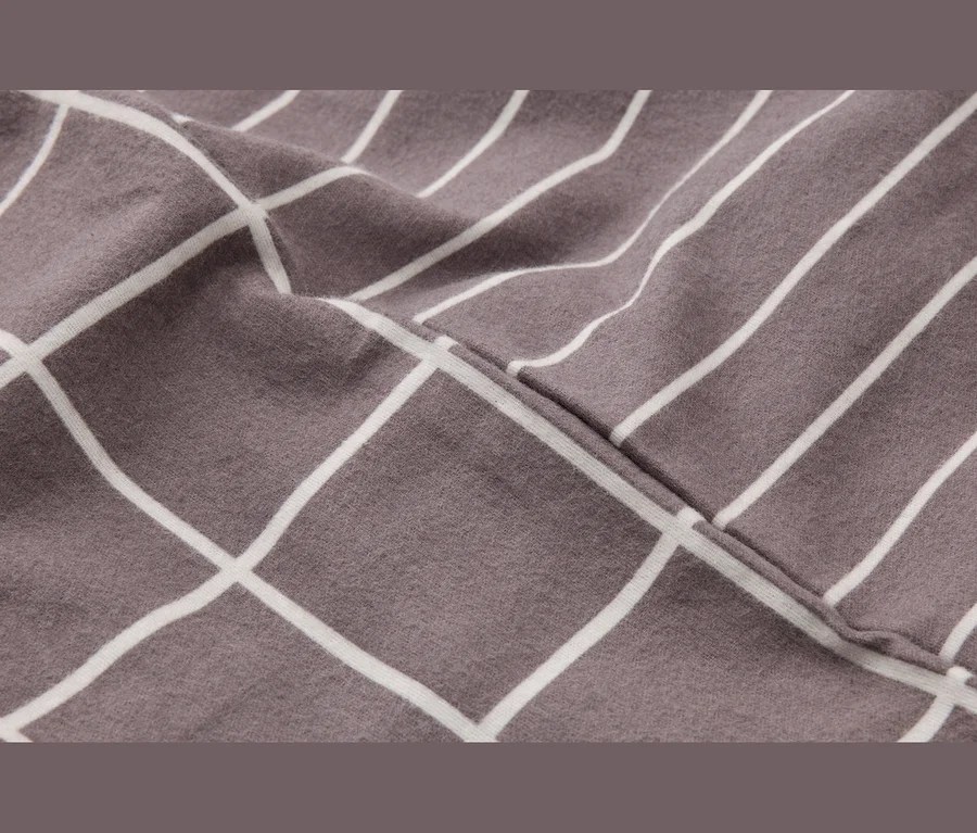 Tissu gris-brun avec des motifs de grille et de rayures parallèles blanches, séparés par une couture diagonale.