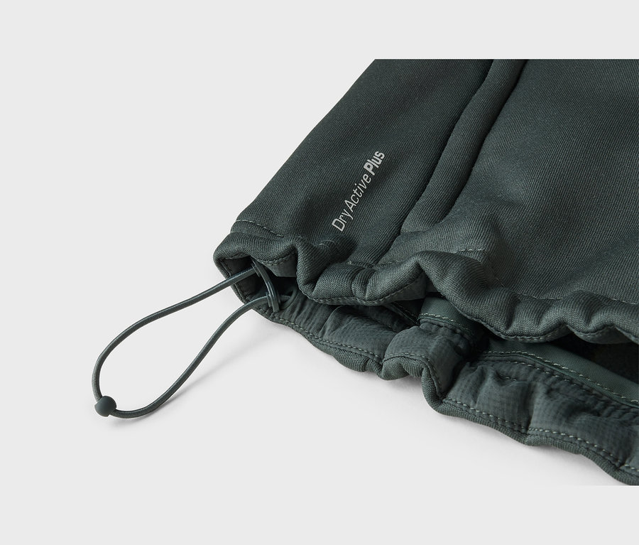 Gros plan sur un tissu vert foncé, probablement un vêtement de sport, avec un cordon de serrage et le texte « DryActive Plus ». Le tissu est froncé autour du cordon, qui possède un arrêt sombre et forme une boucle.