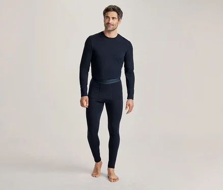 Homme portant un haut thermique à manches longues bleu foncé et un legging thermique assorti, debout pieds nus et souriant légèrement.
