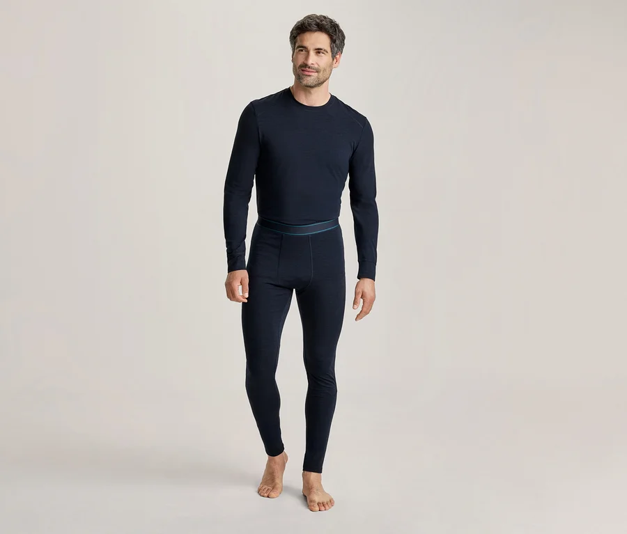 Homme portant un haut thermique à manches longues bleu foncé et un legging thermique assorti, debout pieds nus et souriant légèrement.
