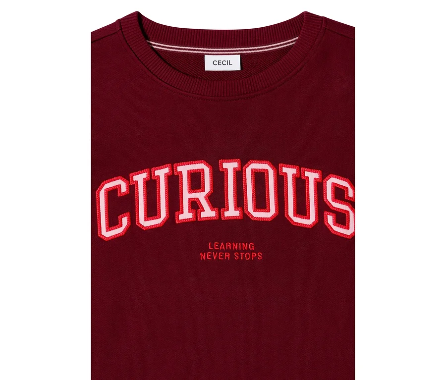 Sweatshirt CECIL bordeaux avec le grand lettrage brodé rouge et blanc « CURIOUS » et « LEARNING NEVER STOPS » en dessous.