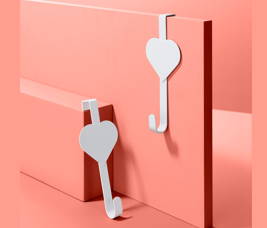Deux crochets de porte blancs avec un design de cœur sur un fond rose corail.