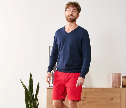 Un homme portant un pull bleu et un short chino rouge.