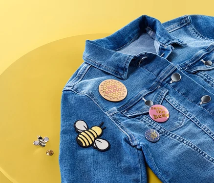 Une veste en jean est posée sur une table jaune et porte un kit de badges et image à repasser.