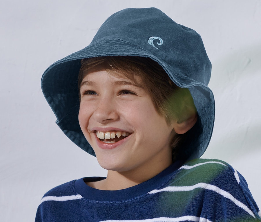 Un garçon souriant est assis avec un haut rayé bleu et blanc et un chapeau de pêcheur enfant.