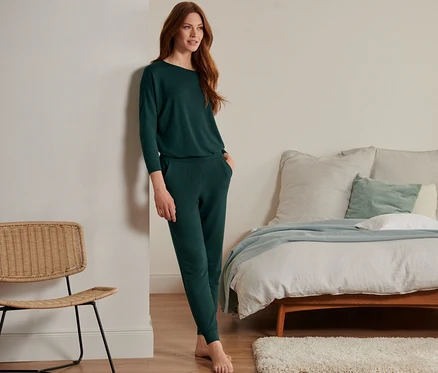 Une femme appuyée contre un mur porte un pantalon de survètement d'intérieur vert foncé en mélange modal et soie.