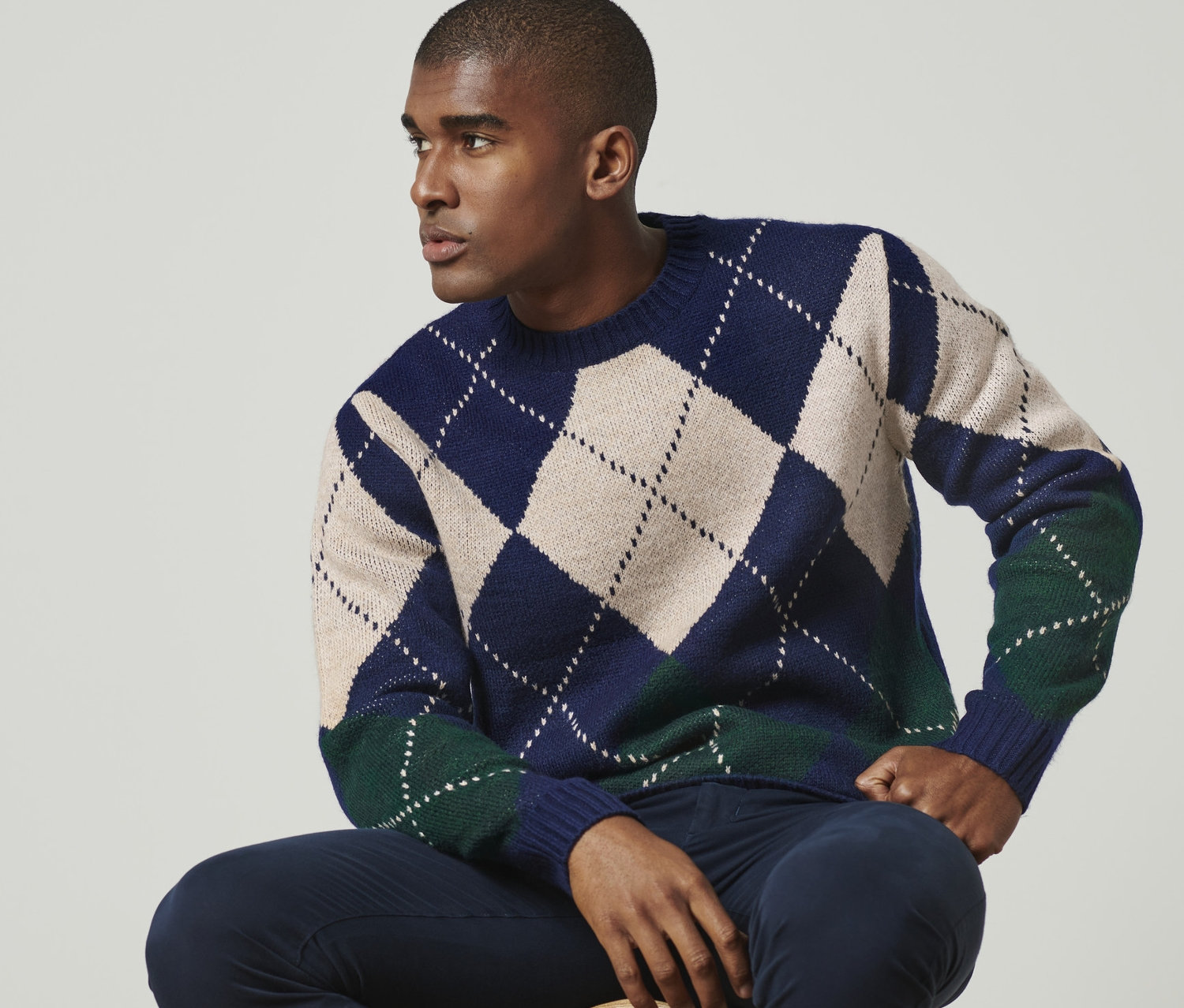 Un homme est assis sur un tabouret et porte un pull en maille.