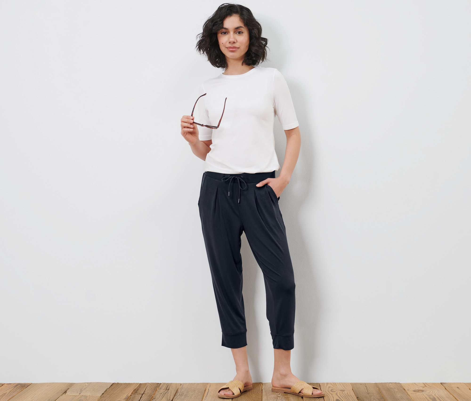 Femme posant sur un plancher en bois en t-shirt blanc et pantalon 3/4 en jersey.