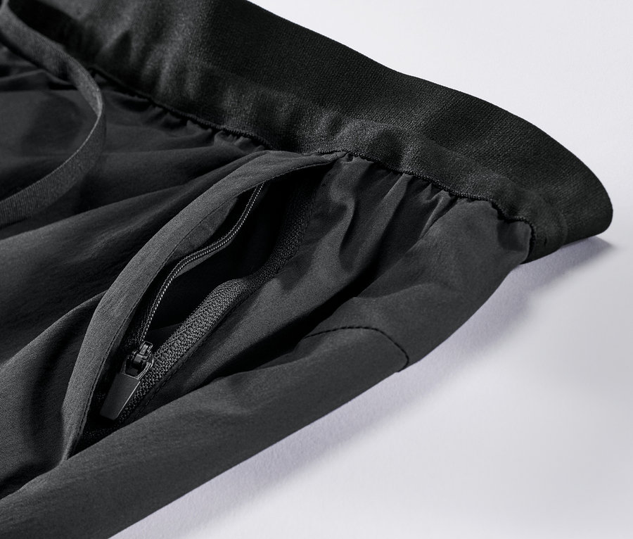 Gros plan sur un pantalon technique noir avec une poche zippée.