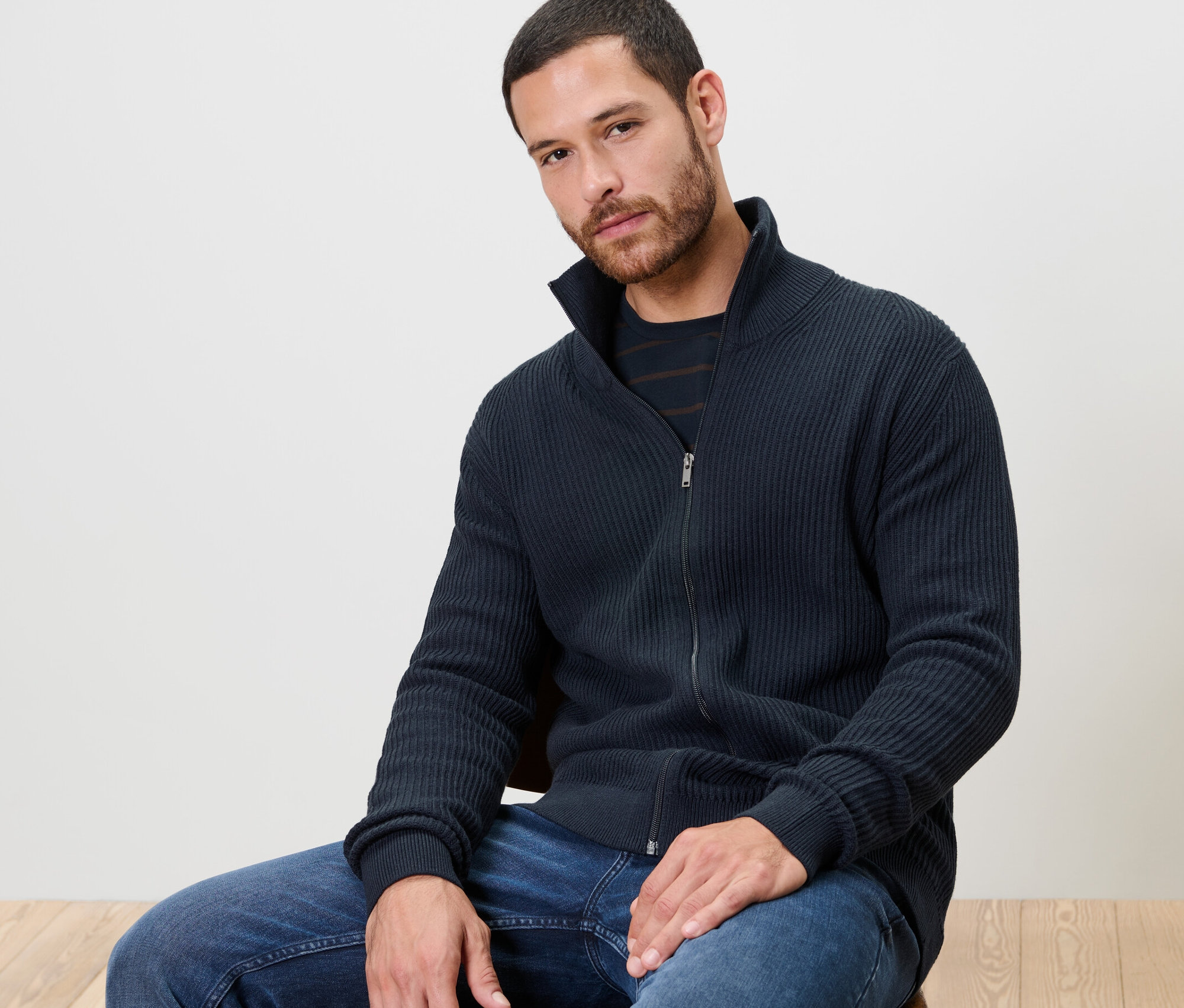 Un homme est assis sur une chaise et porte une jaquette en maille bleu marine.