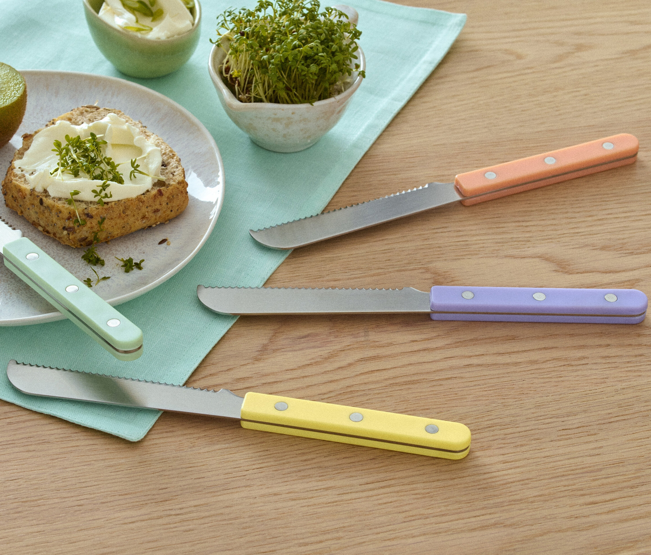 Assiette avec kiwi, pain avec tartinade et cresson à côté de 4 couteaux à petit-déjeuner.