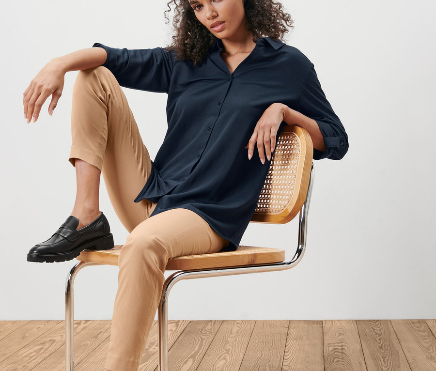 Une femme est assise sur une chaise et porte un chemisier en jersey piqué bleu foncé.