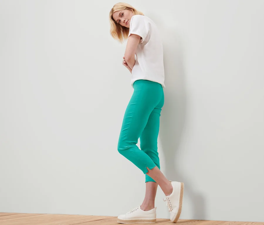 Femme posant en pantalon stretch 7/8 turquoise, t-shirt blanc et chaussures blanches.