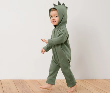 Un enfant en combinaison en sweat avec motif dinosaure appliqué marche sur un plancher en bois.
