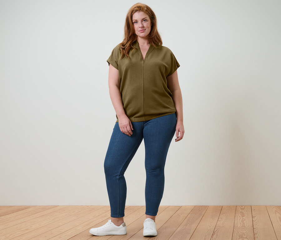 Une femme pose en studio portant une blouse avec encolure en V et un jegging.