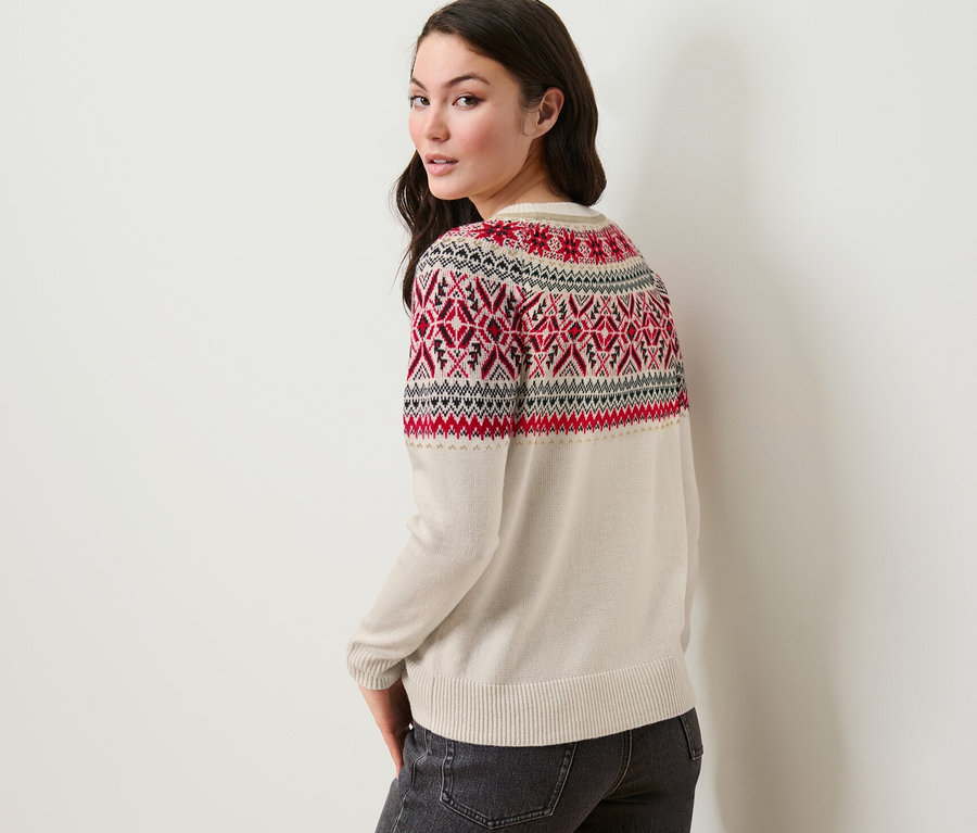 Une femme regardant par-dessus son épaule portant un pull en maille de style norvégien et un jean.
