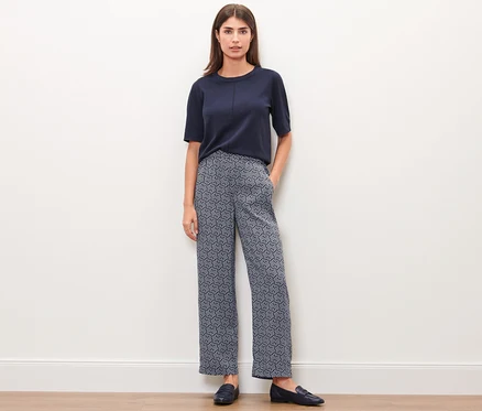 Une femme debout devant un mur blanc porte un haut bleu marine et un pantalon tissé imprimé intégral.