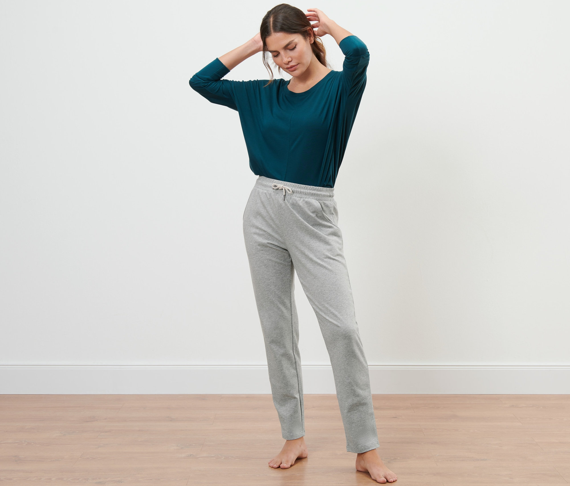 Femme posant en pantalon de jogging gris et haut bleu-vert.