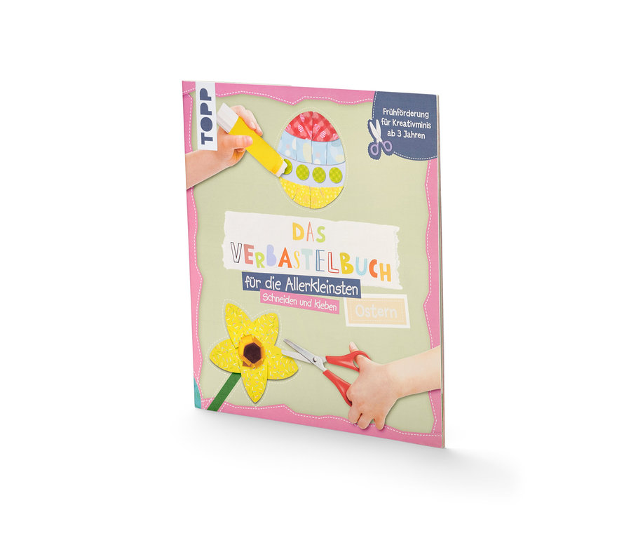 Des mains d'enfants avec de la colle et des ciseaux près du livre « Das Verbastelbuch für die Allerkleinsten – Ostern » (en allemand).