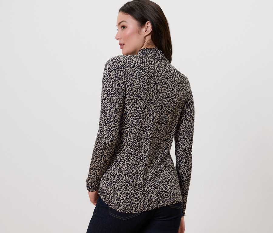 Une femme, dos à la caméra, porte une blouse imprimée à col montant et un jean foncé.