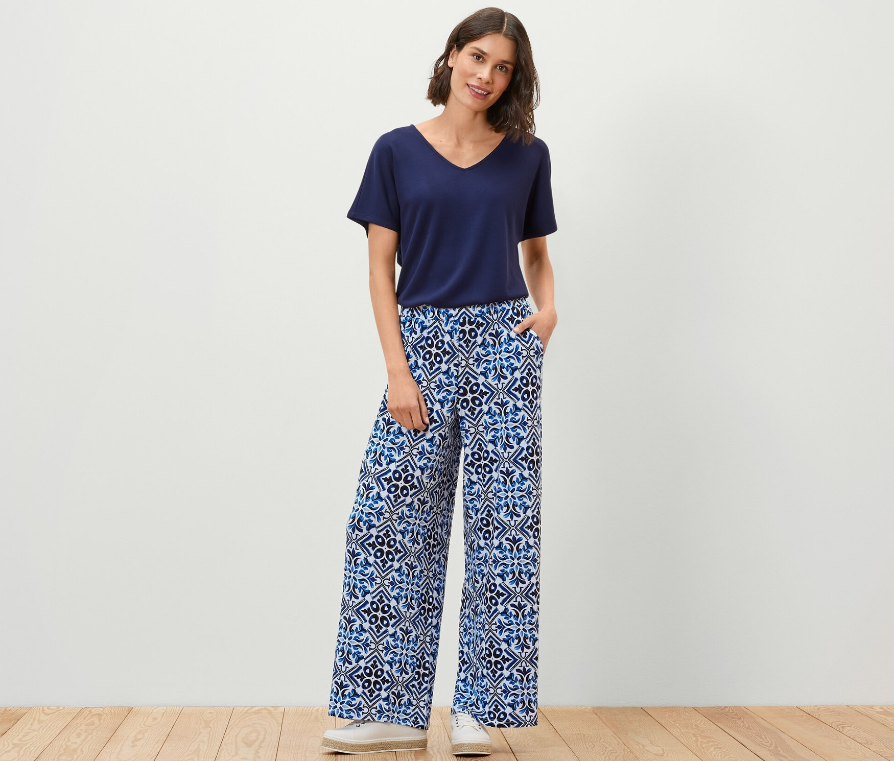 Femme debout, mains dans les poches d'un pantalon palazzo imprimé, bleu.