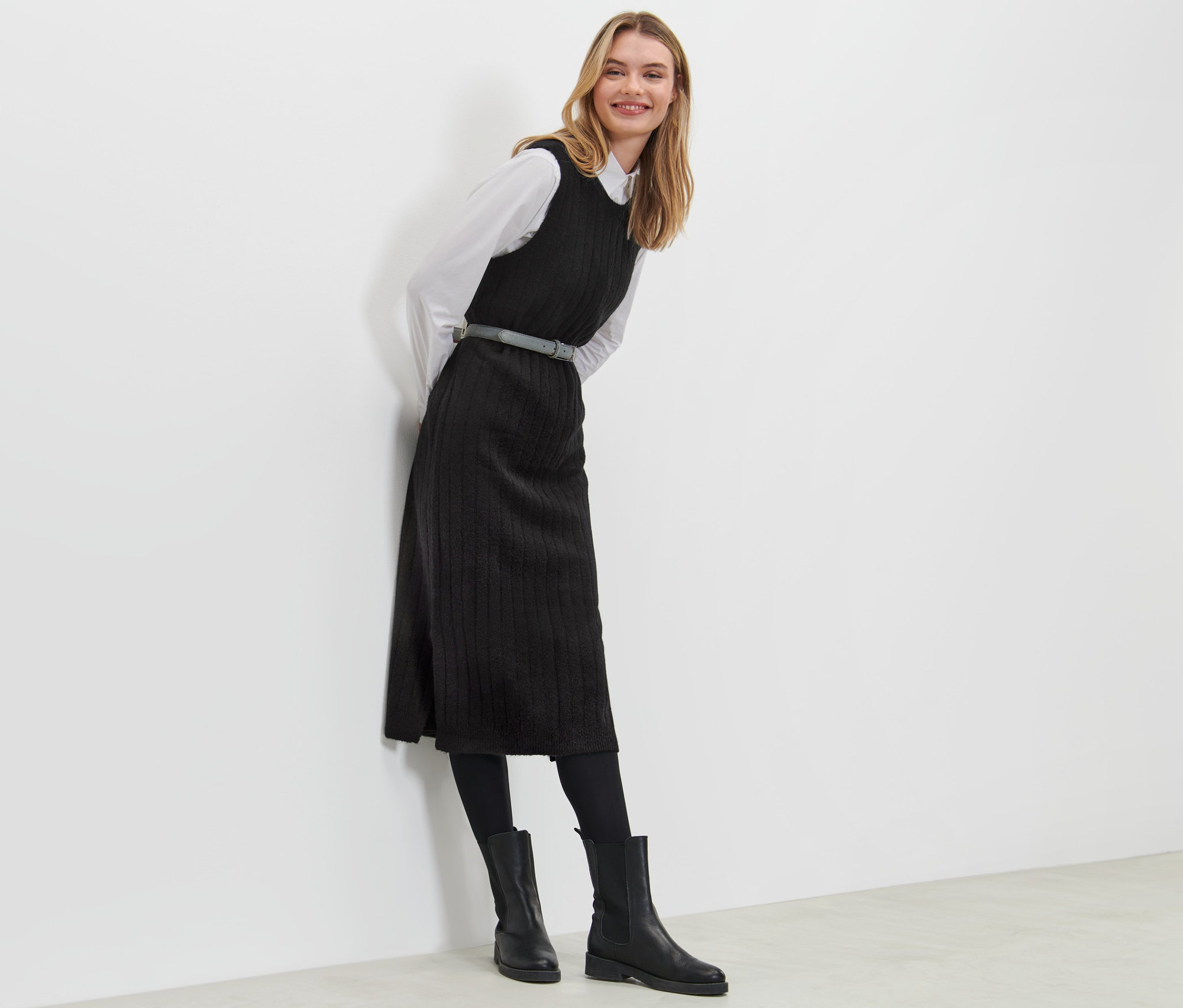 Femme appuyée contre un mur portant une robe noire en tricot côtelée.