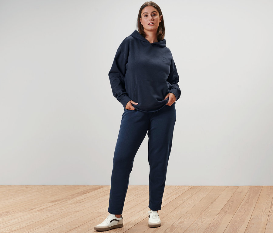 Femme posant en sweat à capuche bleu marine, pantalon de survêtement et baskets en cuir.