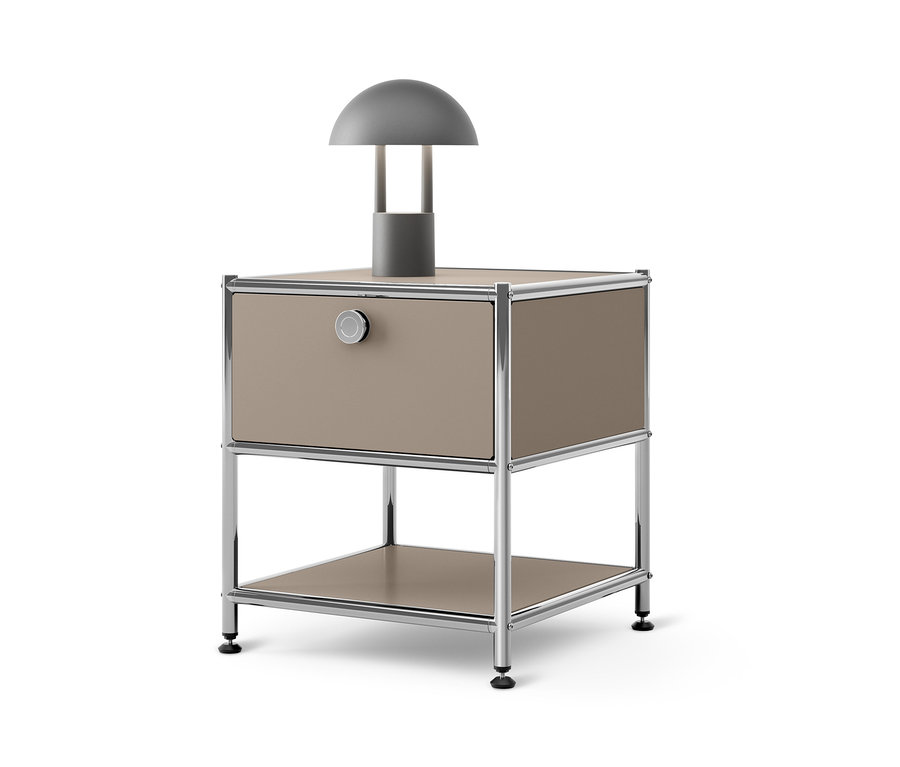 Une lampe grise est posée sur une table d'appoint avec tiroir en métal « CN3 » beige.