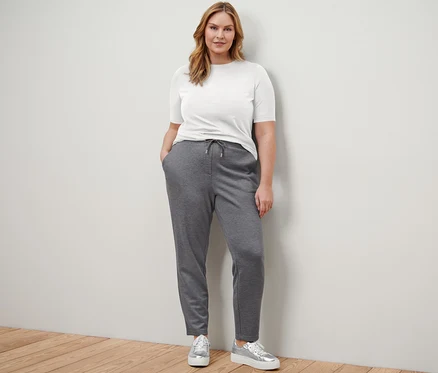 Une femme debout portant un t-shirt demi-manches Basic blanc, un t-shirt demi-manches Basic bleu foncé, un pantalon de jogging et des sneakers à plateau en cuir.