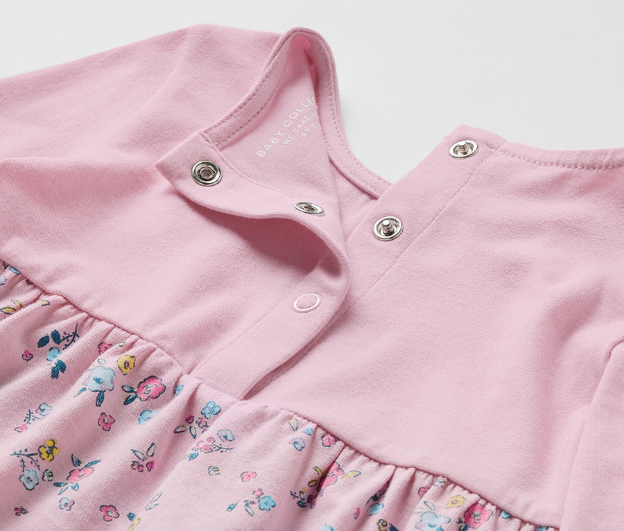 Gros plan sur une robe en jersey rose pour bébé avec un imprimé floral.
