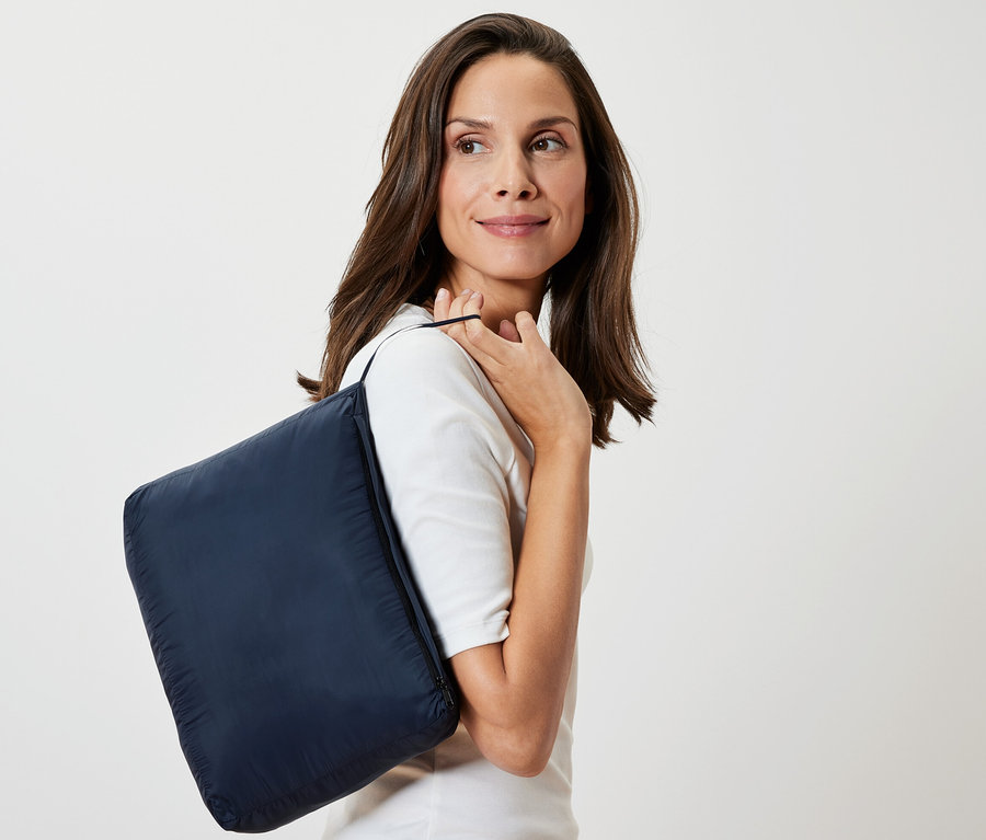 Femme portant une couverture de voyage bleu foncé "Couverture de voyage ultralégère" sur l'épaule.