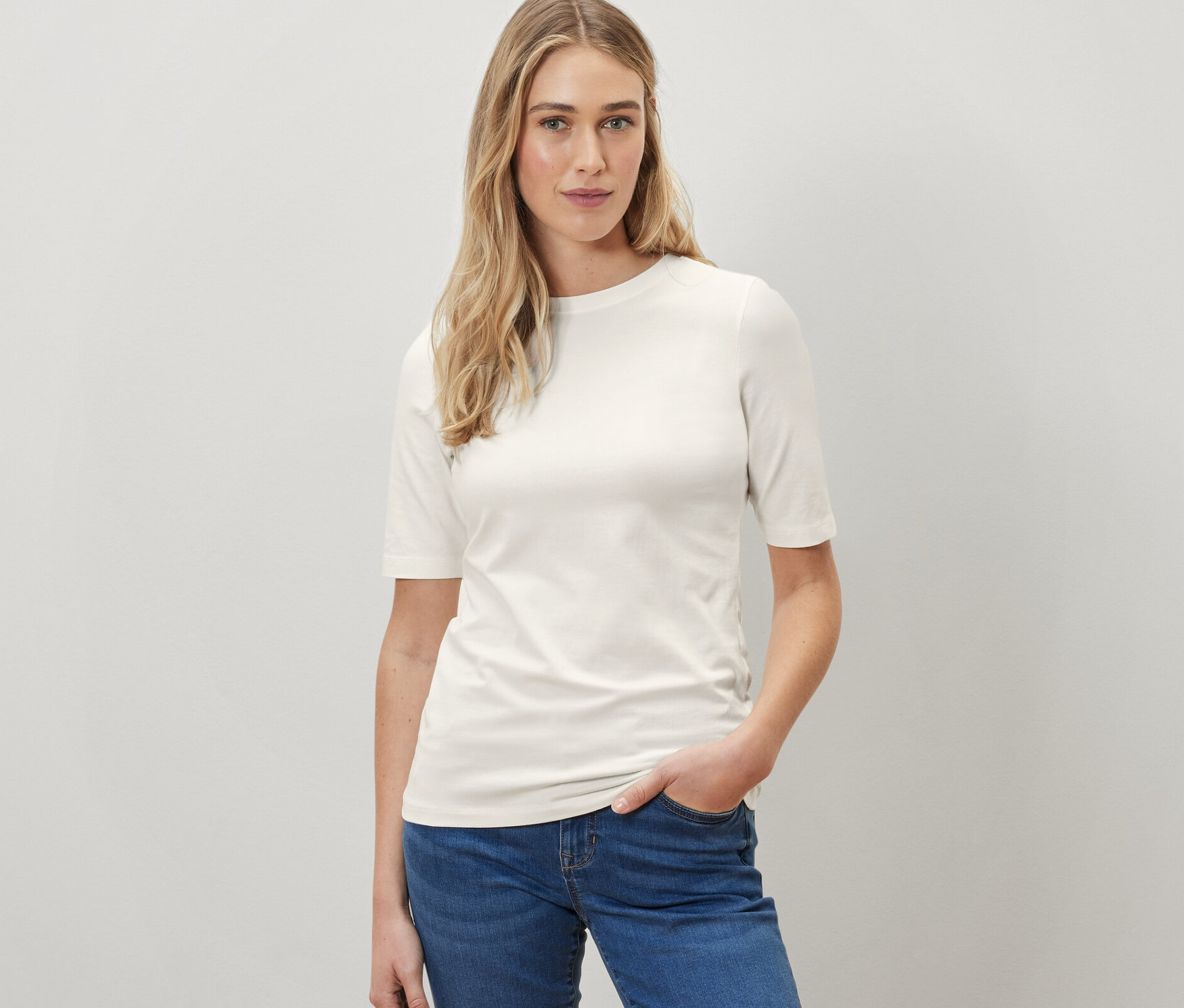 Femme posant en t-shirt crème à manches courtes et jean bleu.