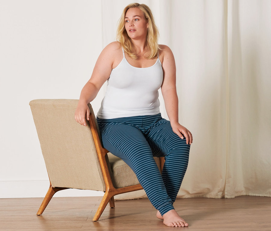 Femme assise sur une chaise portant un caraco blanc (2 caracos, blanc) et un pantalon rayé.