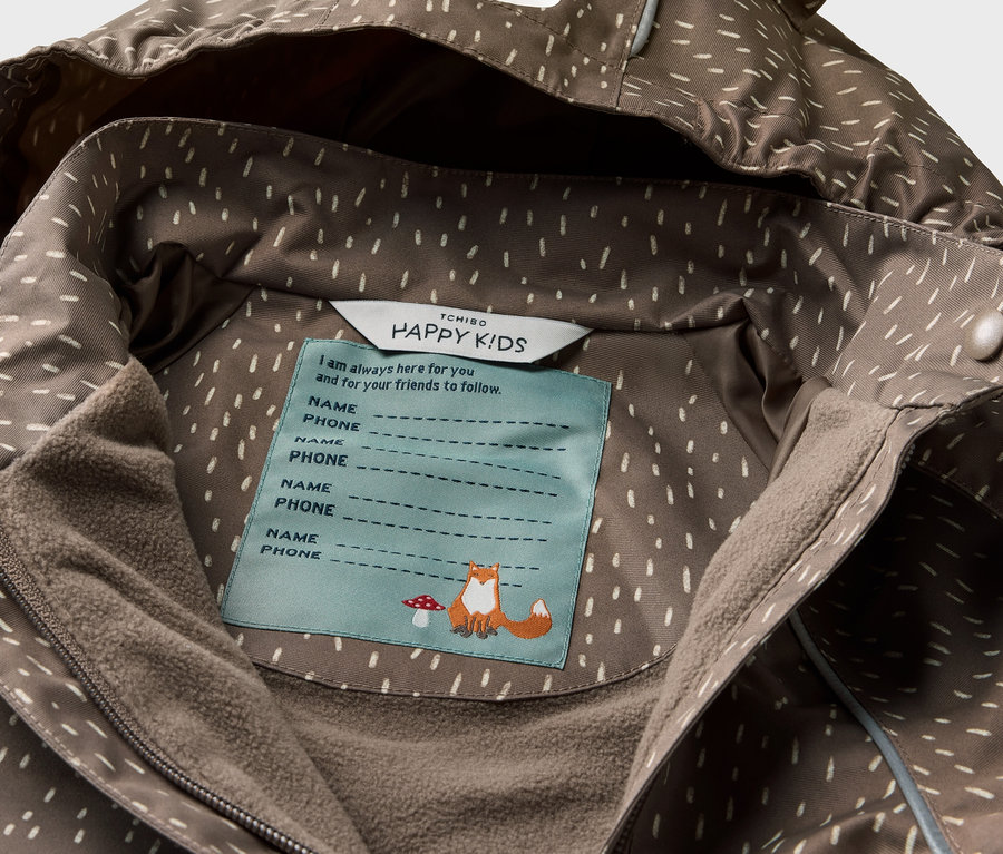 Gros plan sur une veste de pluie thermique pour enfant avec une capuche d'ours et une étiquette intérieure.