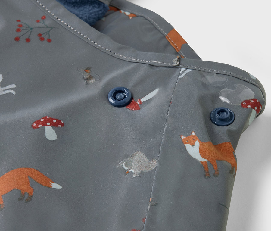 Gros plan sur un pantalon de pluie thermique pour enfants avec des éléments réfléchissants et un imprimé renard et champignon.